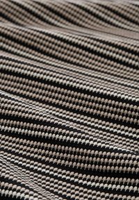 Textiel met een geweven patroon van zwarte, beige en crème strepen. De textuur lijkt zacht en iets verhoogd, met afwisselende kleuren.