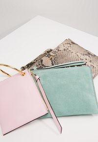 Tre portafogli: uno in pelle rosa con anello dorato, uno in suede verde con tracolla e uno con motivo a serpente in toni neutri.