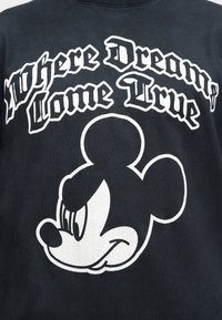 Μαύρο πουκάμισο με λευκό κείμενο «Where Dreams Come True» πάνω από ένα περίγραμμα του χαμογελαστού προσώπου του Mickey Mouse σε λευκό.