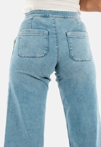 Jeans de cintura alta en azul claro, hechos de denim, que presentan dos bolsillos traseros con bordes curvados y costuras visibles. Diseño de pierna ancha destacado.