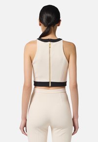 Top corto crema con bordo nero, dotato di una cerniera dorata sul retro e una silhouette aderente. Tessuto liscio, design senza maniche.