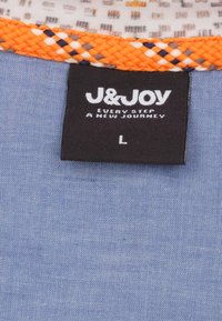 Blauwe stof met een gestructureerde weefsel, voorzien van een oranje gevlochten rand. Een zwart label toont het merk "J&JOY" en maat "L."