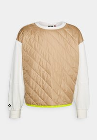 Sudadera acolchada beige con mangas blancas. Presenta costuras diagonales, puños acanalados y un detalle en verde neón en el dobladillo.
