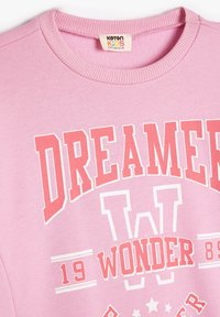 Felpa in cotone rosa chiaro con collo a girocollo a coste, che presenta grafiche testuali bianche e corallo "DREAMER" e "WONDER" e accenti di design a forma di stella.