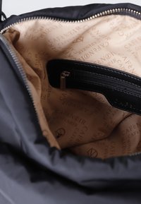 Czarna torba materiałowa o gładkiej fakturze i srebrnym zamkiem. Wnętrze ma beżowe wykończenie z powtarzającym się napisem "Café Noir" oraz kieszonkę na zamek.