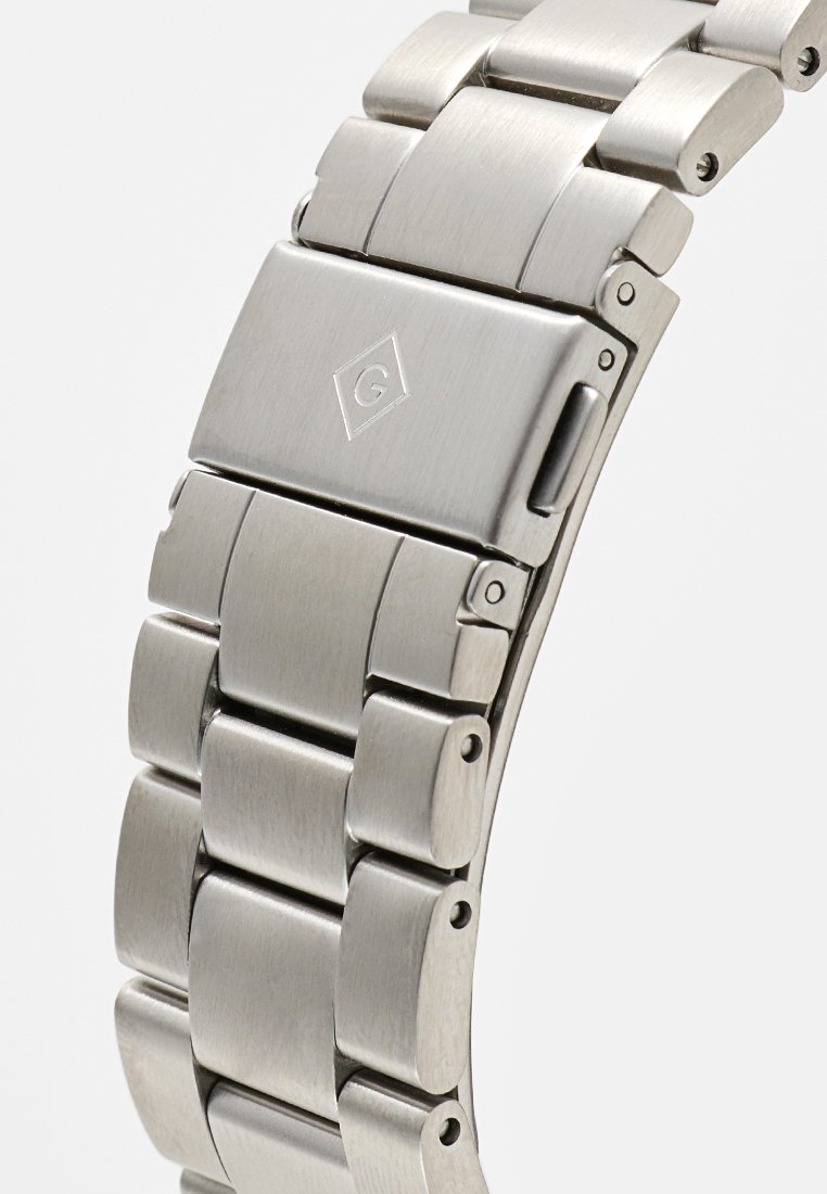 Correa de reloj de acero inoxidable plateado con textura cepillada, eslabones rectangulares y un cierre geométrico con un logotipo en relieve.