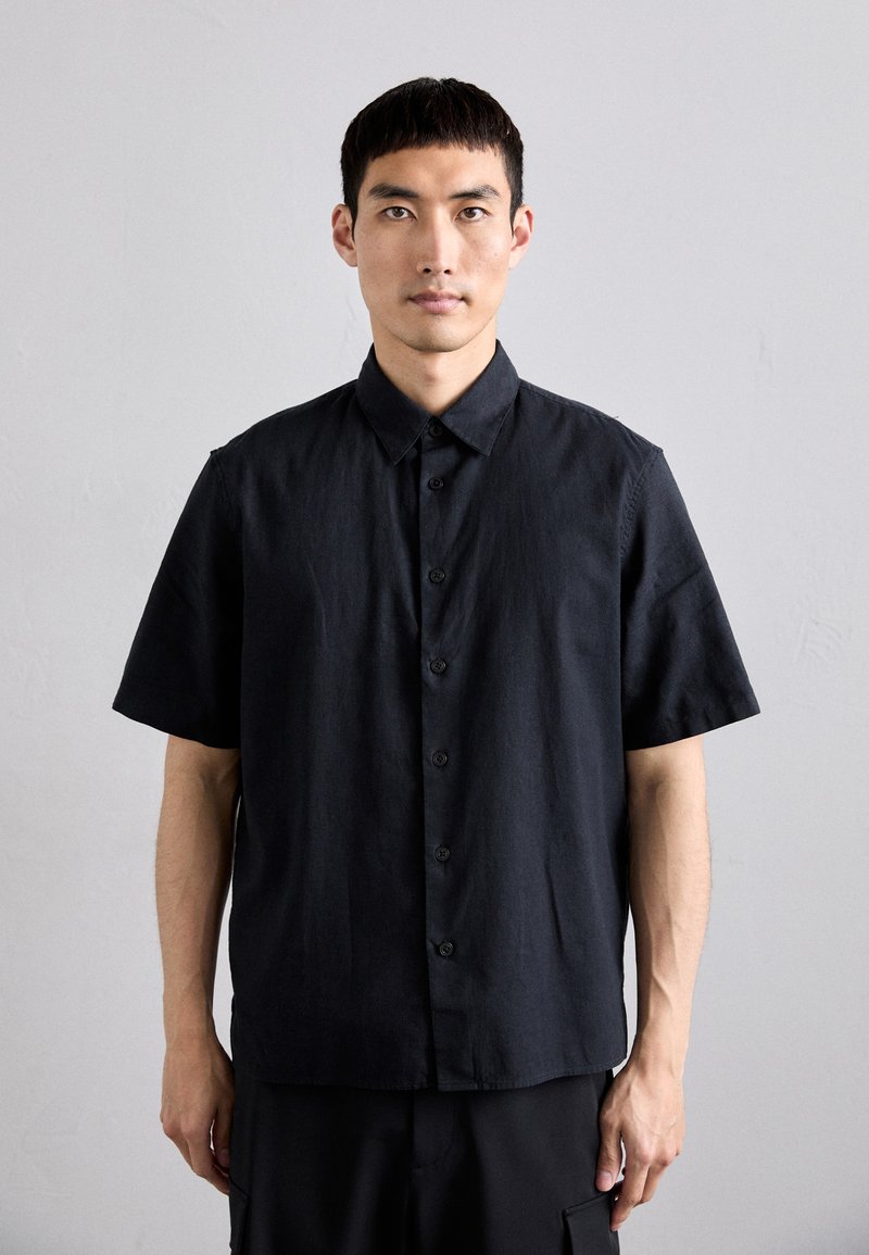 Krátky rukáv, čierna tlačná košeľa vyrobená z ľahkého materiálu. Obsahuje špicatý golier a jemnú textúru.