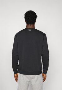 Sort sweatshirt med rund halsudskæring, ribbede manchetter og nedre kant. Har et lille logo mærke på den bageste halsudskæring. Bæres med grå sweatpants.