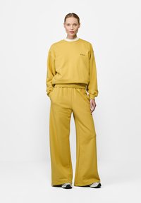 Żółta bluza z suwakiem i szerokie spodnie z miękkiej bawełny. Posiada okrągły dekolt i elastyczny pas. Minimalne logo na klatce piersiowej.