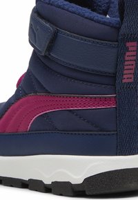 Zapatilla alta de color azul marino con una franja de acento rosa, tela texturizada y una correa de Velcro. Equipada con una suela de goma blanca.