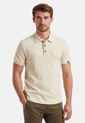 Camisa polo beige de manga corta, con tapeta de botones y un pequeño bolsillo en el pecho. Fabricada con un tejido texturizado, presenta botones oscuros y mangas enrolladas.