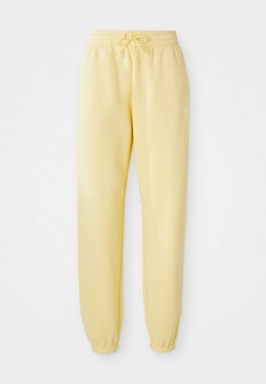 Pantalons de survêtement jaunes avec taille élastique et cordon de serrage. Présente un logo blanc sur le côté gauche et des poignets élastiques aux chevilles.
