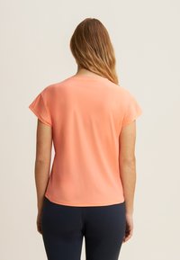 Camiseta de manga corta, ligera, en suave tejido color coral, con textura lisa, escote redondeado, corte entallado, combinada con pantalones azul marino.