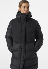 Chaqueta de plumas negra con un cuello alto y bolsillos con cremallera, que presenta secciones acolchadas y una textura suave y reflectante.