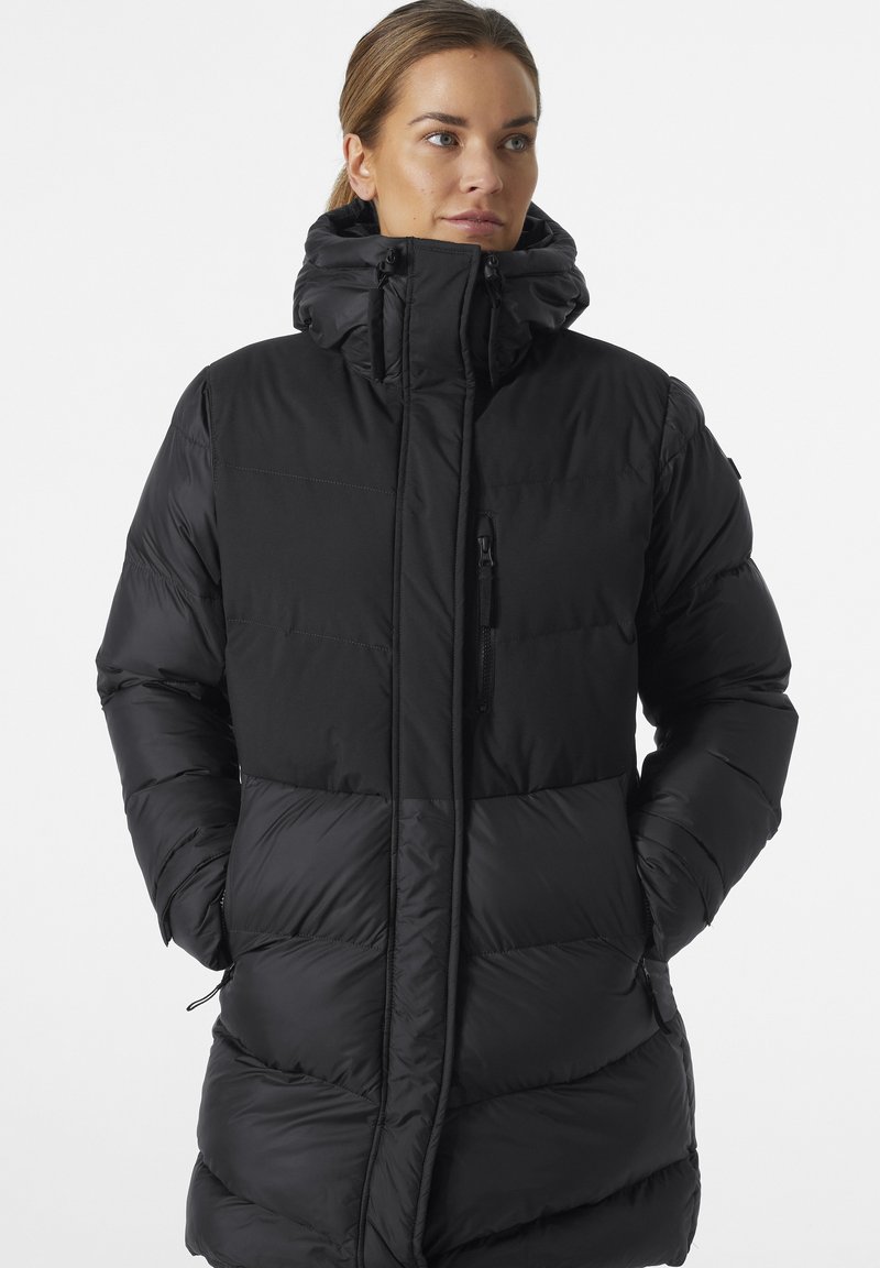 Chaqueta de plumas negra con un cuello alto y bolsillos con cremallera, que presenta secciones acolchadas y una textura suave y reflectante.