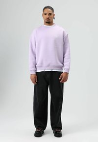 Sweat-shirt lilas avec encolure ronde et poignets côtelés, assorti à un pantalon noir à jambes larges et des chaussures plateformes noires avec des accents roses.