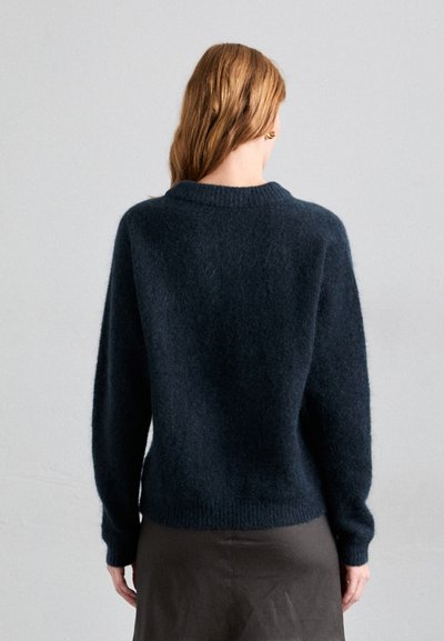 Pull en maille marine foncé avec une texture douce et duveteuse, col rond et manches longues. Bord-côtes à l'ourlet et aux poignets. Modèle de dos.