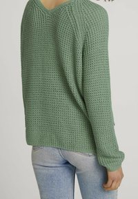 Grön stickad tröja med V-ringning, oversized passform, texturerad tyg och långa ärmar, ihop med ljusblå jeans.