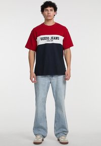 Punased, valged ja tumesinised värvi plokiga T-särk, millel on "GUESS JEANS" logo, kombineeritud heledate siniste teksade ja beežide tossudega. Mugav lõige.