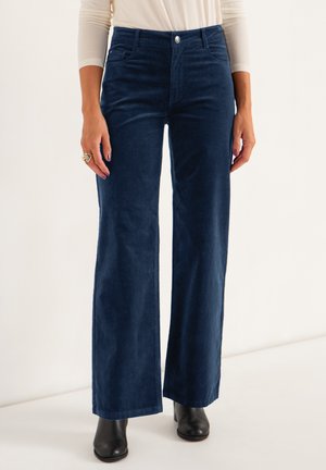 Marineblauwe corduroy wijdvallende broek met voorzakken, knoopsluiting en een gladde textuur, gestyled met zwarte enkellaarsjes.