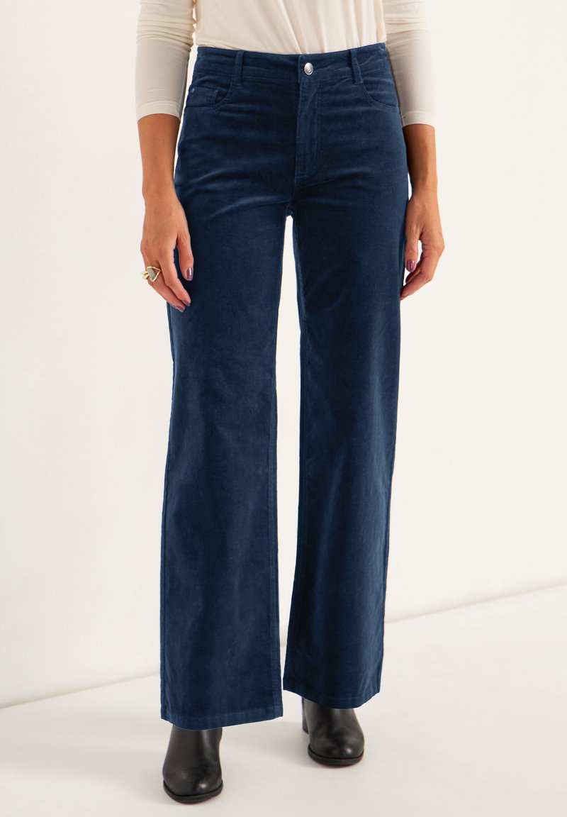 Navy corduroy wide-leg trousers featuring front pockets, a button closure, and a smooth texture, styled with black ankle boots.