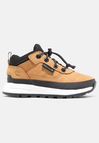 Tann mockasinsneaker med svarta accenter och ett texturerat sula. Har en vadderad krage, elastiska snören och en vit mellansula. Logotyp på sidan.