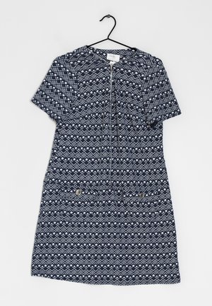 Laivastonsininen lyhythihainen mekko, jossa valkoinen geometrinen timanttikuviollinen printti, etukäytävä, sekä kaksi nappitaskua, ripustettuna mustaan henkariin.