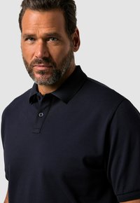 Mörkblå polo skjorta med texturerad krage, korta ärmar och knapplåsning. Har en subtil lyster och klassisk passform.
