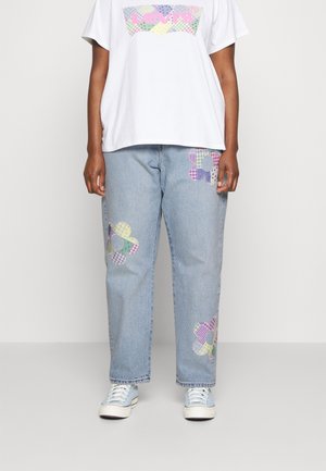 Osoba nosząca jasnoniebieskie dżinsy z pastelowymi kwiatowymi łatkami, białą koszulkę z kolorowym logo Levi's i jasnoniebieskie trampki.