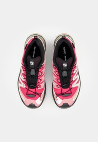 Pink athletic shoes with a textured upper, black accents, laces, and a cushioned sole. Features a logo on the tongue and breathable mesh panels.