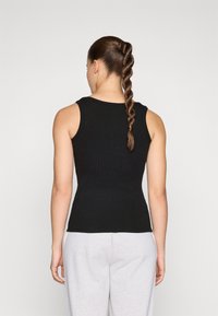 Must mustriba tank top, sobran lõikega, ümmarguse kaeluse ja varrukateta, kantud hallide dressipükstega.