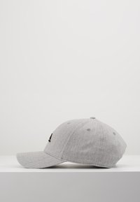 Grå cap med buet skjerm, laget av teksturert stoff, har en svart logo foran, seks ventilasjonsøyler og en knapp på toppen.