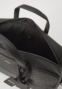 Sac en cuir noir avec extérieur texturé, fermeture zippée et doublure en tissu. L'intérieur comporte une étiquette de logo et un espace de rangement généreux.