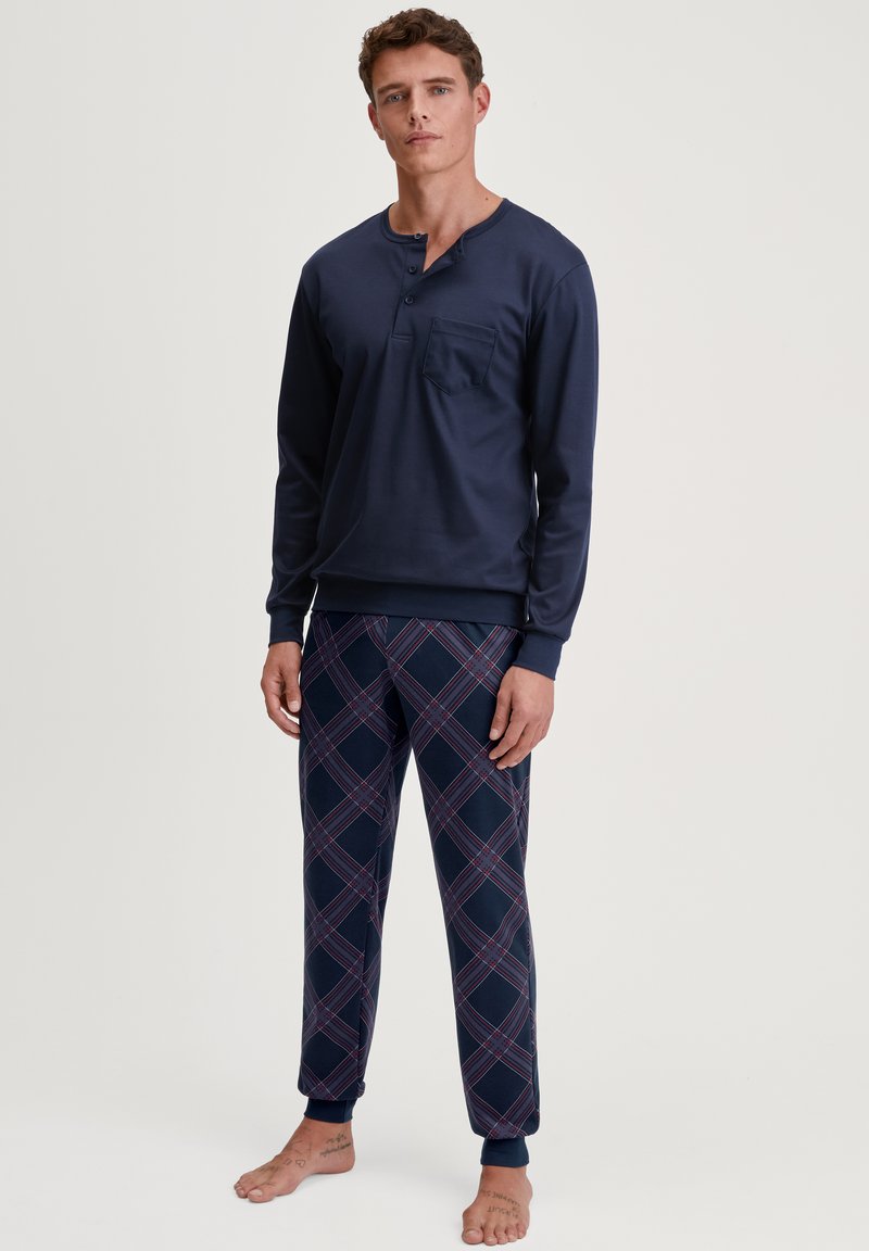 Marineblauw longsleeve shirt met een zak en ronde hals, gecombineerd met een broek met een blokmotief in blauw, rood en wit. Zachte stof, elastische manchetten.