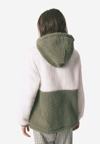 Polarowy pulower w kolorze białym i oliwkowym, z kapturem, teksturowanym materiałem i blokowym designem w luźnym kroju.