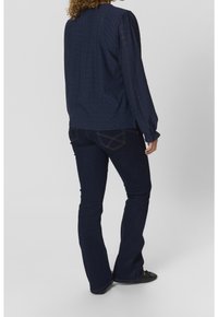 Blouse bleu marine  à manches longues avec un motif texturé, associée à un jean évasé en denim foncé. Tissu doux, encolure ronde et poignets élastiqués.