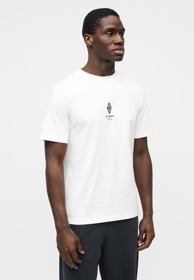 Fehér pamut póló, középen kis fekete logóval. Rövid ujjú, klasszikus környakú kialakítás. Simaságú anyag.