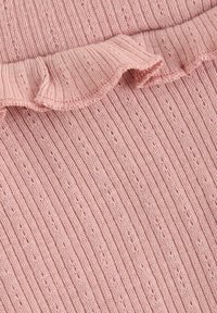 Rosa stickad tyg med vertikal ribbning och en dekorativ volang längs kanten. Texturen verkar mjuk med små mönster genom hela.