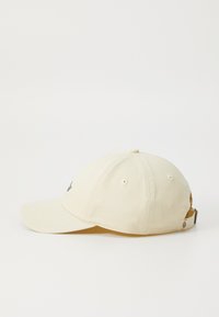 Beige színű pamut baseball sapka ívelt peremmel, hat szellőzőnyílással, hátul állítható pánttal és elöl logóval.