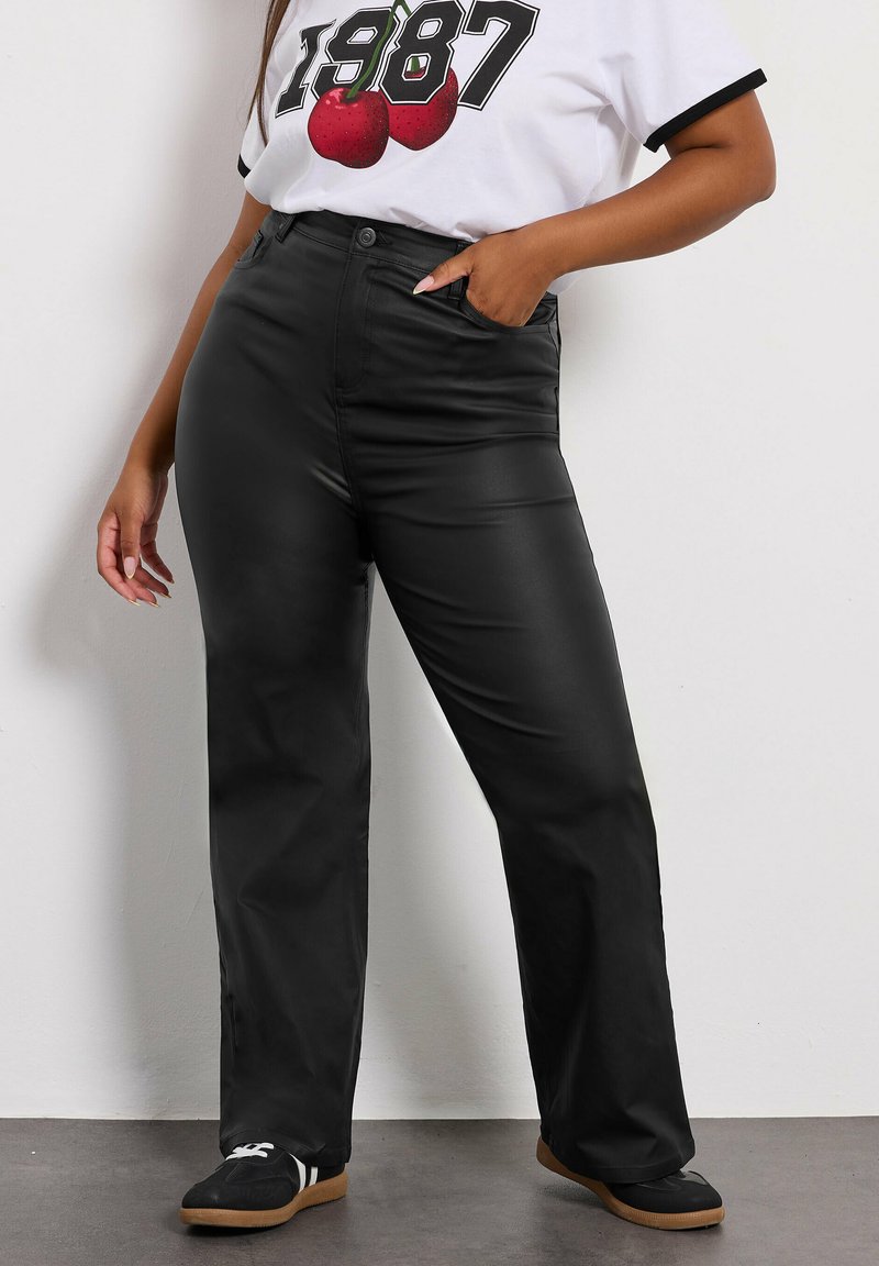 Svarta högmidjade byxor med slät textur och vida ben, kombinerat med en vit t-shirt med grafisk design som har röda körsbär.