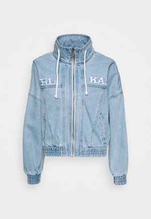 Lyseblå denimjakke med høj krave, hvide snore, frontlynlås, elastiske manchetter og kant samt hvidt broderet delvist tekst på brystet.