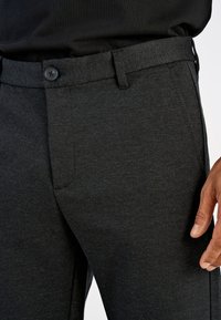 Hallid, tekstuuriga vabaaja püksid, millel on nööp-kinnitusega ees taskud. Omaduseks on istuv vöökohal ja pehme kangas.