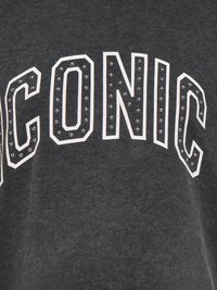 Donkergrijze sweater met het woord "ICONIC" in dikke, witte letters versierd met zilveren studs. Zachte stof met een gladde textuur.