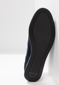 Sula av en svart gummisula med texturerat grepp och "BOSS HUGO BOSS" pr präglat nära hälen, placerad mot ett vitt hörn.