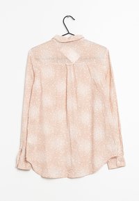 Blush pink long-sleeve blouse with a dotted pattern, buttoned cuffs, and a back pleat; lightweight, sheer fabric, rounded hem.