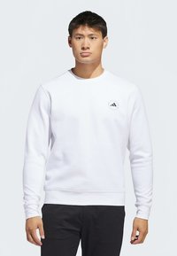 Vit sweatshirt med rund halsringning, långa ärmar och ribbade muddar. Har en liten svart logotyp på vänster bröst. Slät textur.
