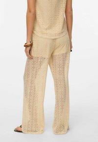 Lichtbeige kanten broek met een cirkelpatroon en een losse pasvorm. De stof is semi-doorzichtig en gestructureerd, wat mooi aansluit bij een bijpassend top.
