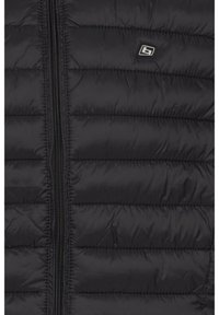 Schwarze Pufferjacke mit vertikalen Steppmustern, Reißverschluss in voller Länge und kleinem Logo auf der oberen linken Seite. Glatte, glänzende Textur.