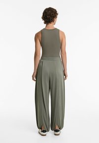 Top a righe verde oliva abbinato a pantaloni larghi e svasati con dettagli plissettati e spacchi alla caviglia. Completato con sneakers a suola bianca.
