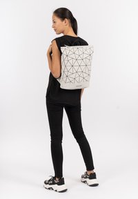 Zaino bianco con motivo geometrico e accenti triangolari neri, realizzato in materiale sintetico, con design a risvolto e spallacci regolabili.